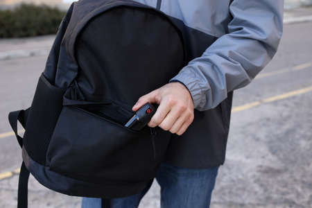 Man putting pepper spray into backpack outdoors, closeupの写真素材