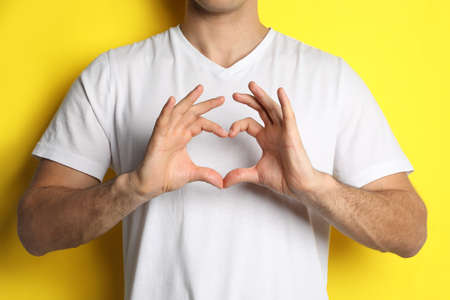 Man making heart with hands on yellow background, closeupの写真素材