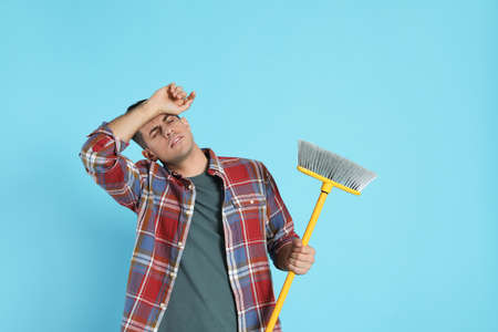 Tired man with yellow broom on light blue background