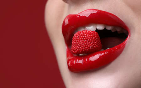 Closeup view of beautiful young woman with perfect lips makeup eating candy on red backgroundの写真素材