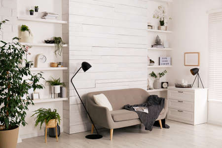 Stylish living room interior with comfortable sofa, wall shelves and beautiful decor elements