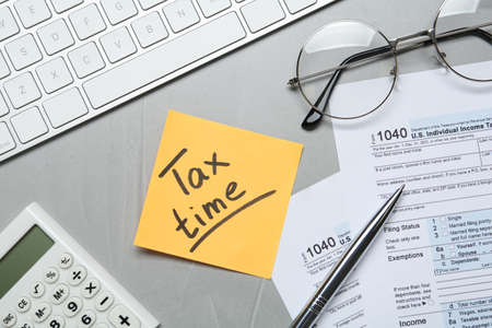 Reminder note with words Tax Time, documents, computer keyboard and calculator on gray table, flat...