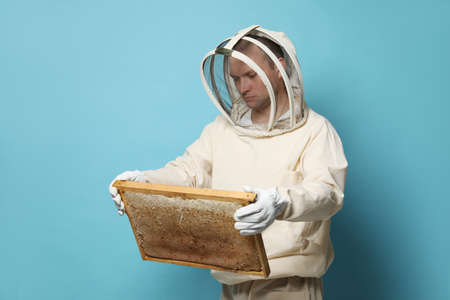 Beekeeper in uniform holding hive frame with honeycomb on light blue backgroundの写真素材