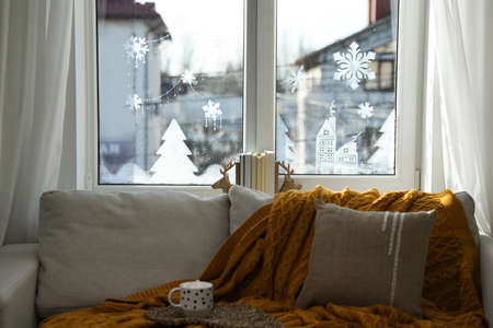 Cup of hot drink on sofa near window with beautiful drawing at home. christmas decorの写真素材