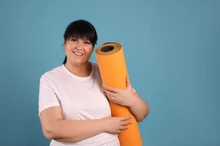 Happy overweight mature woman with yoga mat on light blue background. Space for textの写真素材