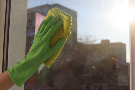 Young woman cleaning window glass with rag at home, closeup. Space for text