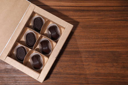 Tasty chocolate candies in box on wooden table, top view. Space for textの写真素材