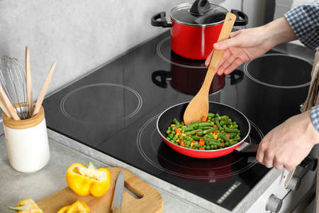 Woman cooking tasty vegetable mix in frying pan at home, closeup
