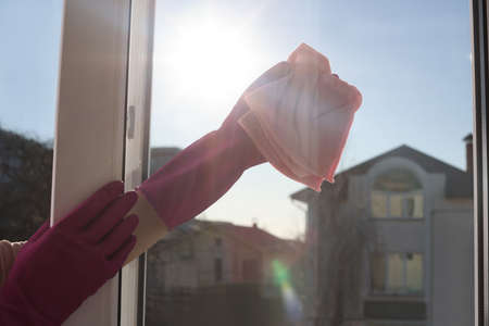 Young woman cleaning window glass with rag at home, closeupの写真素材
