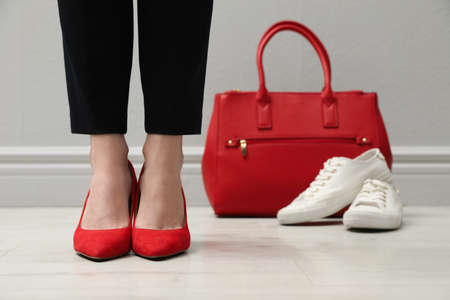 Businesswoman in high heel shoes standing near comfortable sneakers and bag indoors, closeupの写真素材