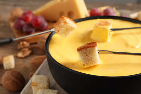 Dipping pieces of bread into tasty cheese fondue at table, closeupの写真素材