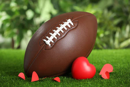 American football ball and hearts on green grass against blurred backgroundの写真素材