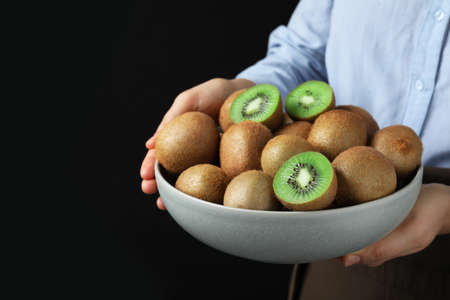 Woman holding bowl with fresh ripe kiwis on black background, closeup. Space for textの写真素材