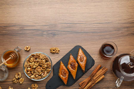 Delicious sweet baklava with walnuts, honey, cinnamon and hot tea on wooden table, flat lay. Space for textの写真素材