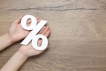 Woman holding paper percent symbol cutout on wooden background, top view. Space for textの写真素材