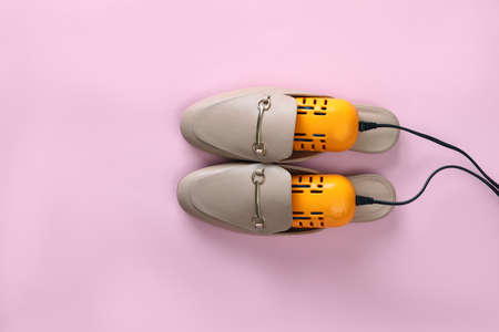 Pair of stylish shoes with modern electric footwear dryer on pink background, top view. Space for...