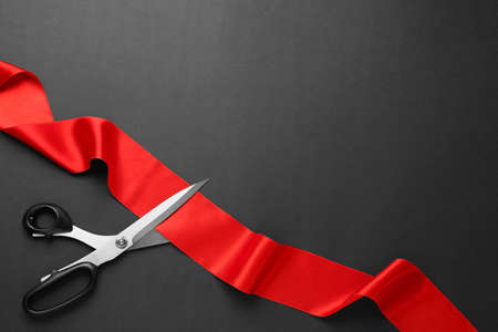 Red ribbon and scissors on black background, top view. Space for textの写真素材
