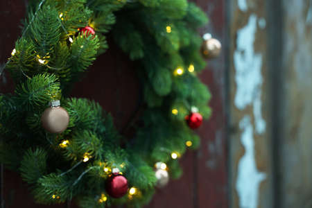 Beautiful Christmas wreath with baubles and string lights hanging on wall, closeup. Space for textの写真素材