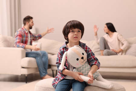 Sad little boy with toy and his arguing parents on sofa in living roomの写真素材
