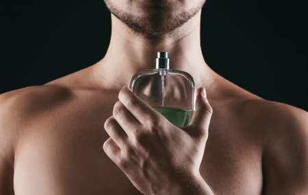 Handsome man with bottle of perfume on black background, closeupの写真素材