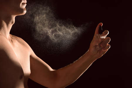 Young man applying perfume on black background, closeupの写真素材
