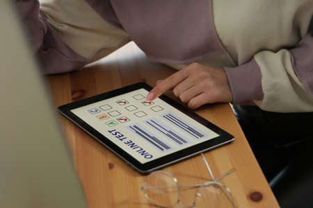 Woman taking online test on tablet at desk, closeupの写真素材