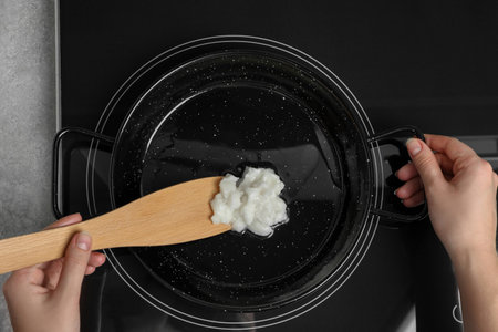 Woman cooking with coconut oil on induction stove, top viewの写真素材