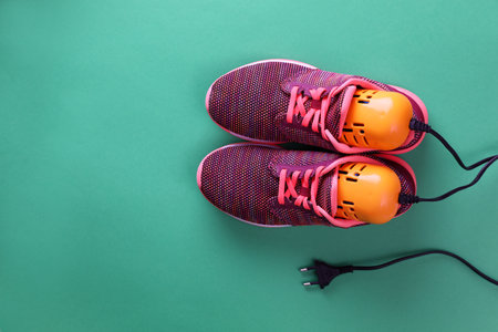 Pair of stylish sneakers with modern electric shoe dryer on green background, top view. Space for textの写真素材