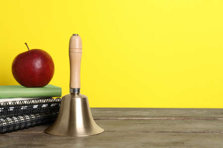 Golden school bell, apple and notebooks on wooden table against yellow background, space for textの写真素材