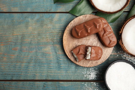 Delicious milk chocolate candy bars with coconut filling on blue wooden table, flat lay. Space for textの写真素材