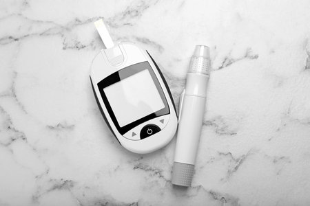 Glucometer and lancet pen on white marble table, flat lay. Diabetes testing kitの写真素材