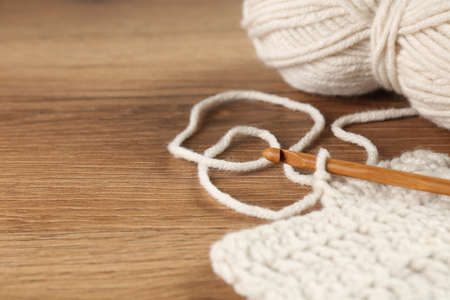 Knitting and crochet hook on wooden table, closeup. Space for text