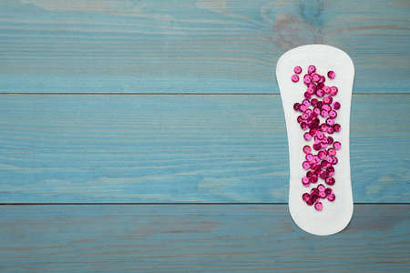 Sanitary pad with pink sequins on turquoise wooden background, top view and space for text....
