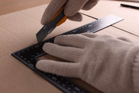 Worker cutting cardboard with utility knife and ruler, closeupの写真素材
