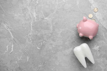 Ceramic model of tooth, piggy bank and coins on gray table, flat lay with space for text. Expensive...