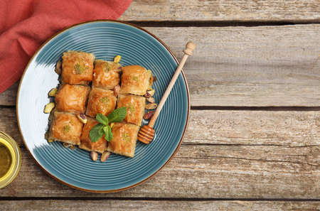 Delicious baklava with pistachios, honey and mint on wooden table, flat lay. Space for textの写真素材