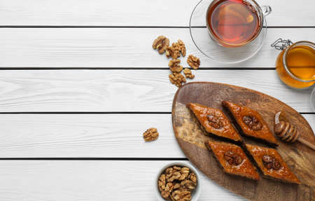 Delicious sweet baklava with walnuts, honey and hot tea on white wooden table, flat lay. Space for textの写真素材
