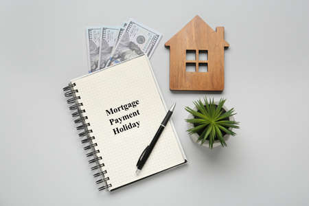 Notebook with words Mortgage Payment Holiday, house model, plant and money on light gray background, flat layの写真素材