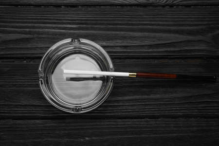 Cigarette in elegant holder and clean glass ashtray on black wooden table, top viewの写真素材