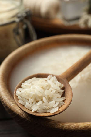 Wooden bowl with soaked rice and spoon on table, closeup