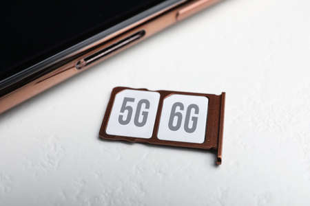 internet concept. 5 and 6G SIM cards in tray with smartphone on white table, closeup