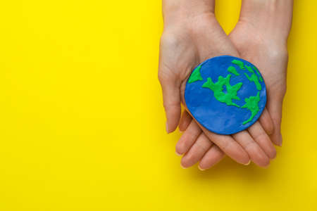 Woman holding plastic model of planet on yellow background, top view with space for text. earth day