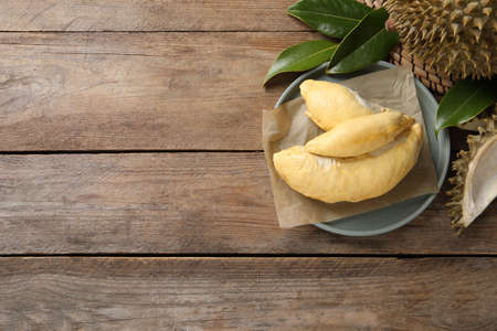 Fresh ripe durians and leaves on wooden table, flat lay. Space for textの写真素材