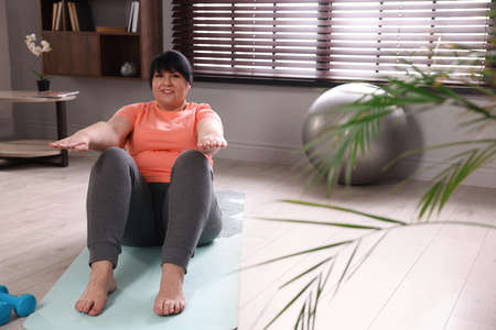 Overweight mature woman doing abs exercise on yoga mat at home, space for textの写真素材