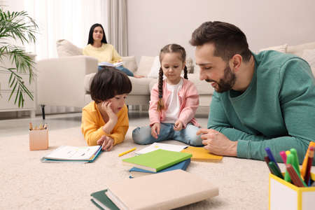 Father playing with his children while mother reading book on sofa in living room