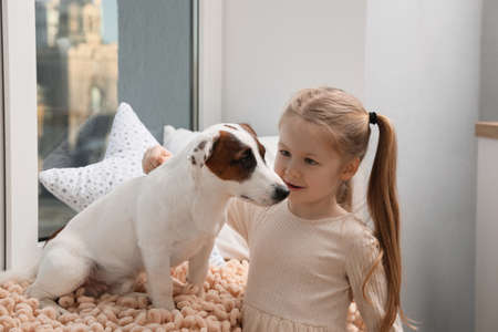 Cute little girl with her dog near window at home. Childhood petの写真素材