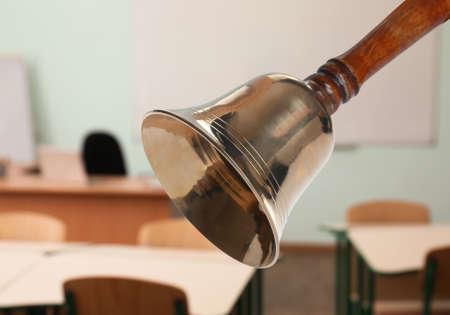 Golden school bell with wooden handle and blurred view of empty classroomの写真素材