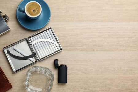 Case with tobacco filter cigarettes, ashtray, lighter and cup of coffee on wooden table, flat lay. Space for textの写真素材