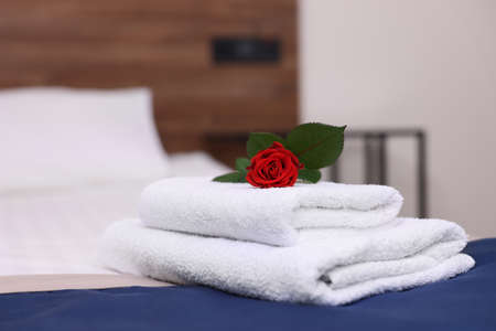 Stack of clean towels with flower on bed in hotel roomの写真素材