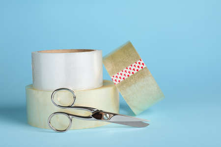 Rolls of adhesive tape and scissors on light blue background. Space for text